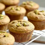 Freshly baked vegan pistachio muffins with a golden-brown crumble topping, served on a wooden board.