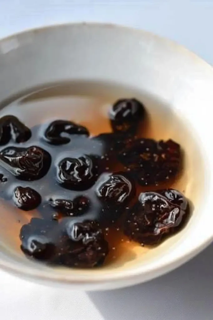 Dried cherries soaking in warm water in a small glass bowl to soften before being added to muffin batter.