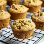 A single vegan pistachio muffin with a bite taken out, revealing its fluffy, moist interior.